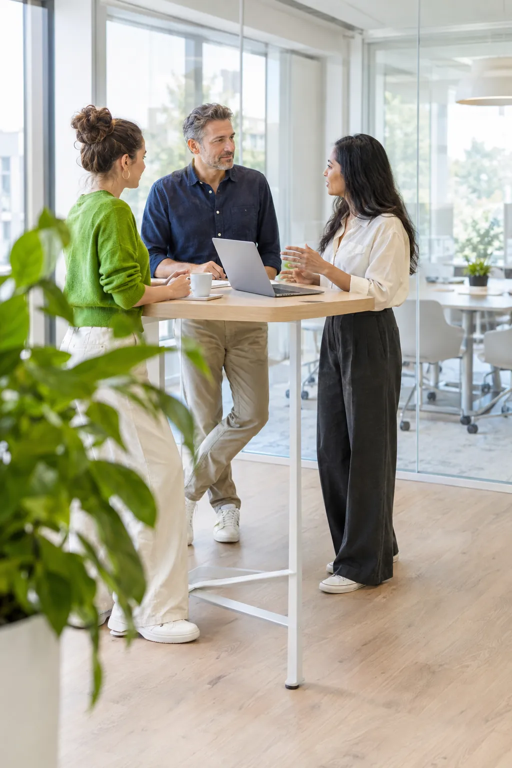 Drei Kolleginnen und Kollegen im Gespräch an einem Stehtisch in einem hellen Büro mit Glaswänden