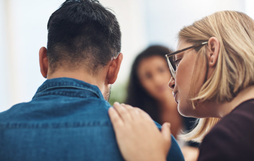 Depression am Arbeitsplatz - Was Unternehmen tun können Teammitglieder stehen einem Kollegen tröstend bei und reden ihm gut zu.