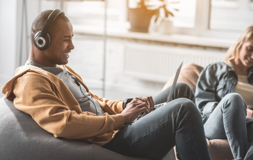 Flexible Arbeitszeiten Zwei Kolleg:innen sitzen in gemütlicher Lounge zusammen und arbeiten teils mit Kopfhörern