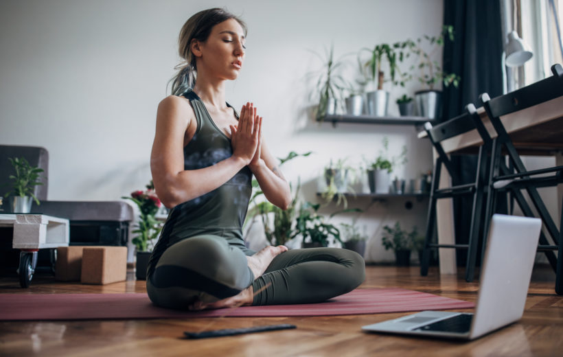 Mithilfe von digitalen Angeboten meditieren kann das Stresslevel im Alltag senken Frau meditiert auf dem Boden vor ihrem Laptop