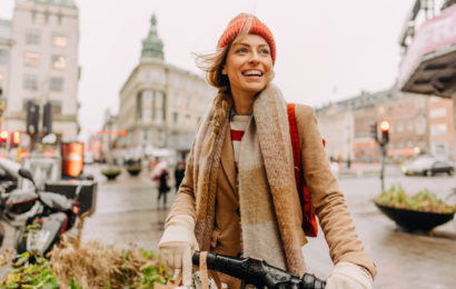 Frau in Winterkleidung fährt lachend auf dem Fahrrad durch die Stadt.