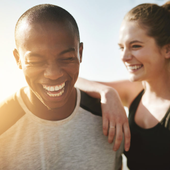 Ein Mann und eine Frau in Sportbekleidung lachen gemeinsam und freuen sich aufs Workout.
