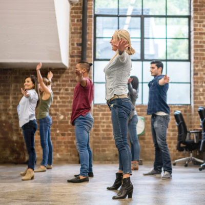 Mehrere Teammitglieder eines Unternehmens führen gemeinsam eine Sportübung im Büro aus.