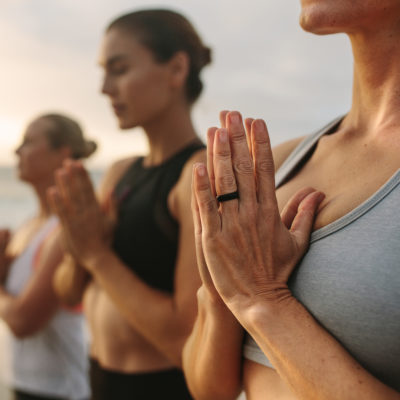 Mehrere Frauen in Sportbekleidung stehen draußen in einer meditierenden Pose.