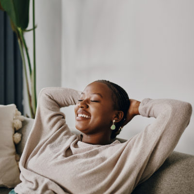 Eine Frau in gemütlicher Bekleidung sitzt entspannt auf einer Couch und lacht.