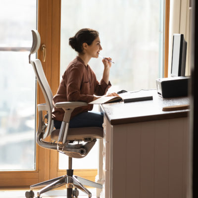 Frau sitzt in ergonomischem Stuhl an leicht angewinkeltem Schreibtisch und arbeitet am Rechner