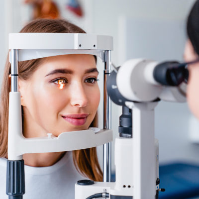Frau an Sehtestgerät wird von Ärztin an den Augen untersucht