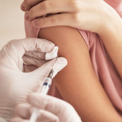 Fachkraft setzt Spritze mit Handschuhen an Arm einer Patientin an und impft.