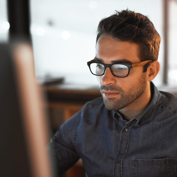 MEDISinn Angebot Augengesundheit Junger Mann mit Brille sitzt im Büro und blickt angestrengt in den Bildschirm