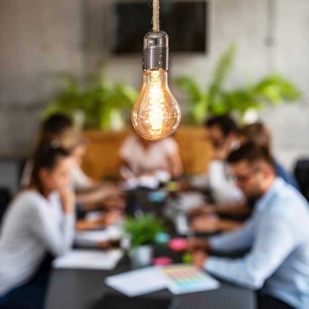 MEDISinn Angebot Change Management Mehrere Mitarbeiter:innen sitzen in einem Kreativworkshop, Fokus auf Glühbirne, d.h. Ideenfindung