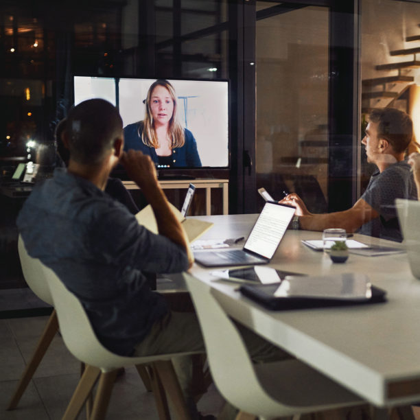 MEDISinn Angebot Führen von internationalen Teams Nächtliches hybrides Meeting im Büro, in das eine Kollegin per Video dazugeschaltet ist,