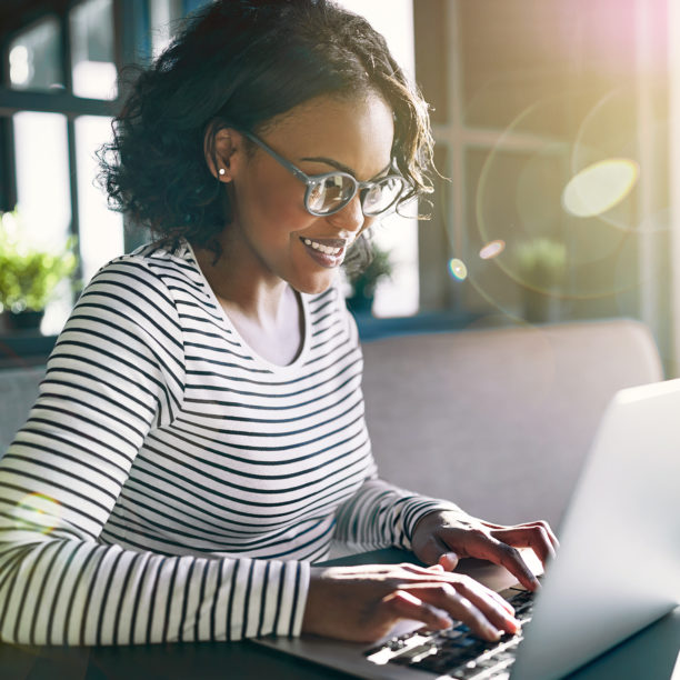 MEDISinn Angebot gesund und leistungsfähig im Homeoffice Junge Frau mit Brille sitzt konzentriert und lächelnd am Laptop im Homeoffice