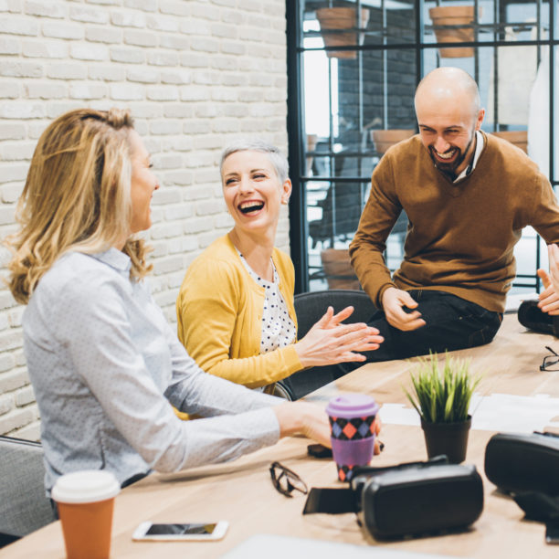 MEDISinn Angebot Kommunikation im Team Zwei Frauen und ein Mann sitzen gemeinsam im Meetingraum, unterhalten sich angeregt und lachen dabei