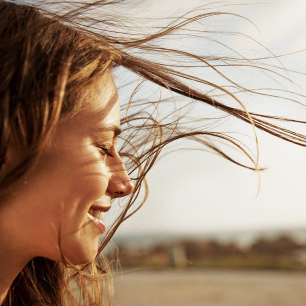 Frau blickt lächelnd zur Seite während der Wind ihr durch die Haare weht.