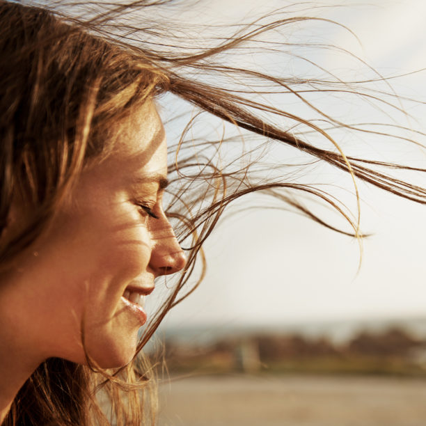 MEDISinn Angebot Resilienz Frau blickt lächelnd zur Seite während der Wind ihr durch die Haare weht.